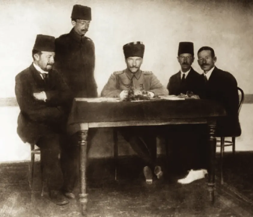 Bir masanın etrafında oturan ve ayakta duran beş kişi; ortada Mustafa Kemal Paşa.