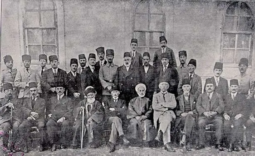 Bir okul binasının önünde, iki sıra hâlinde oturan ve ayakta duran, çoğu fesli kalabalık bir delegeler grubu.
